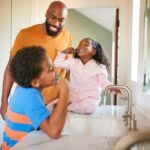 father helping his children brush their teeth